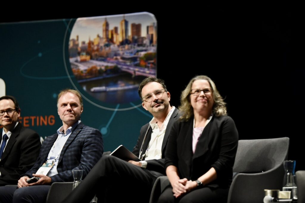 4 people, professionally dressed, sit on a stage on chairs, looking to the right of the photo